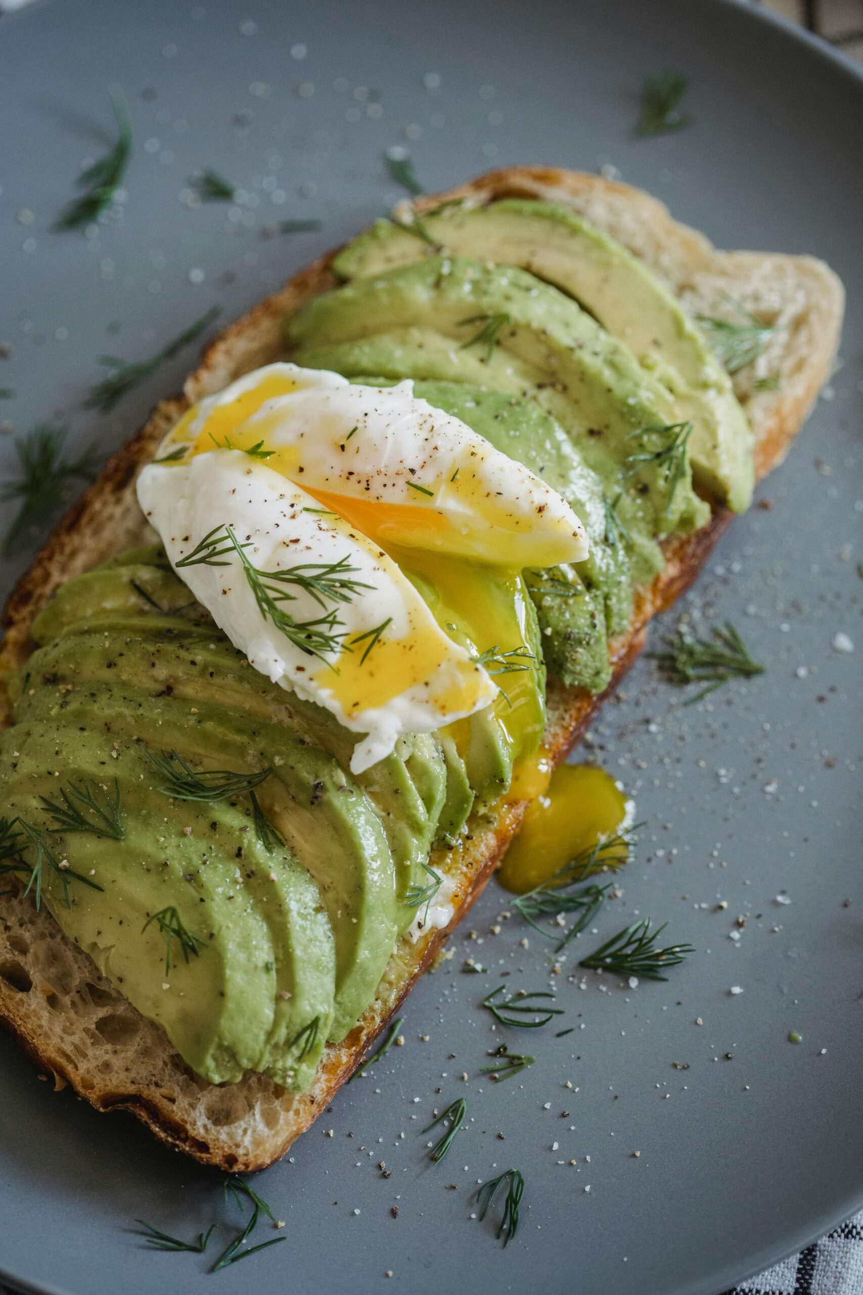 Sliced avocado on toast with a perfectly poached egg and herbs.